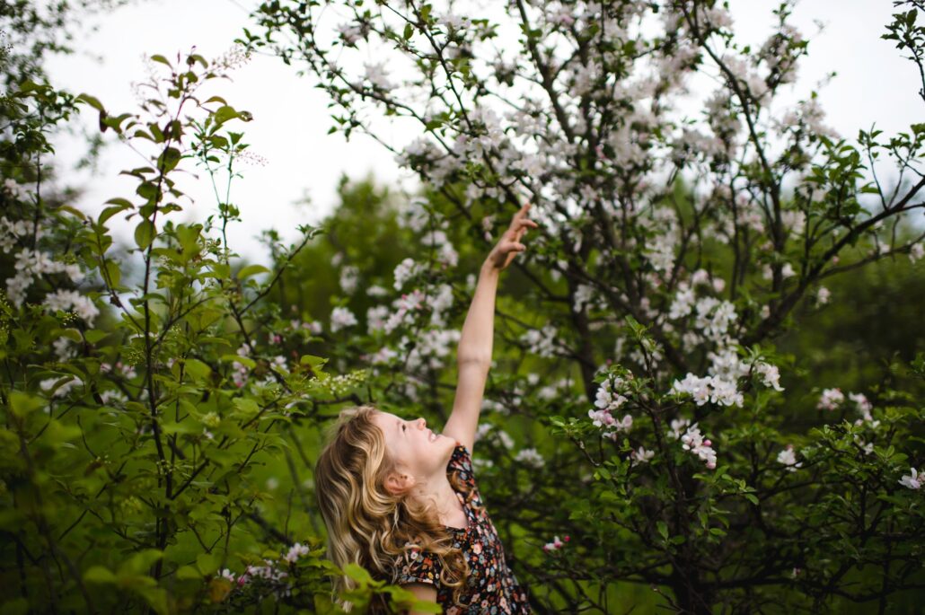 Girl with wavy blond hair reaching up to tree blossom