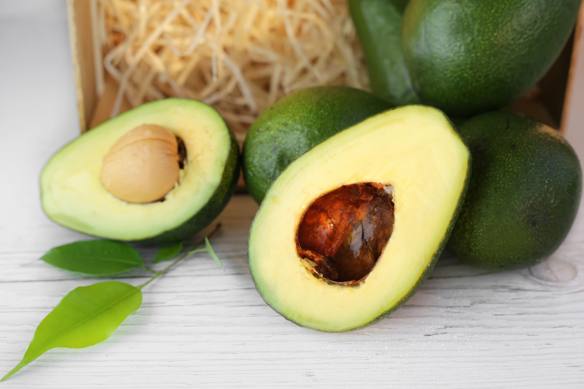 Whole and halved avacado on a light wooden background
